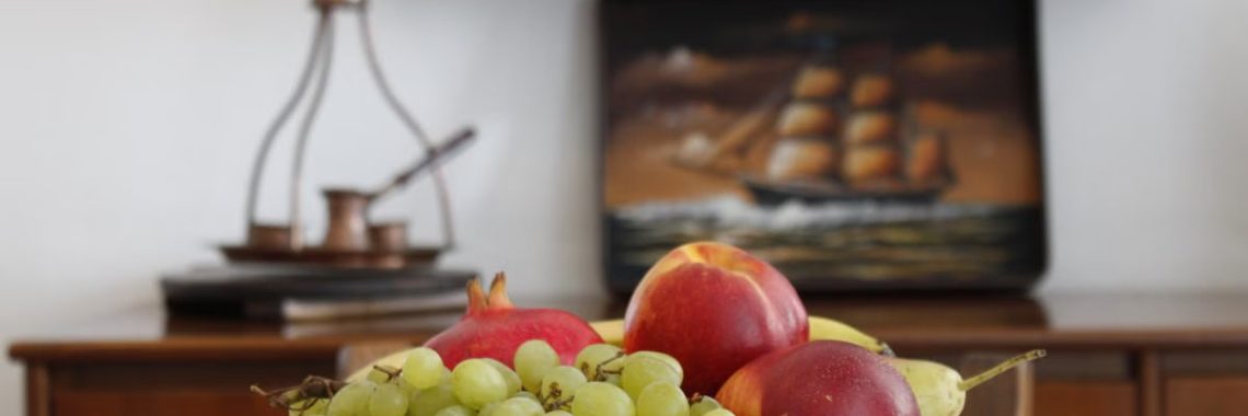 A vibrant bowl of assorted fruits on a table inside a Greek home, showcasing decorative elements.