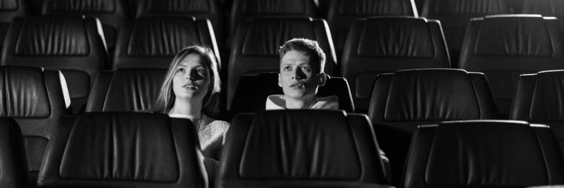 A couple watching a movie in an empty theater with monochrome lighting.